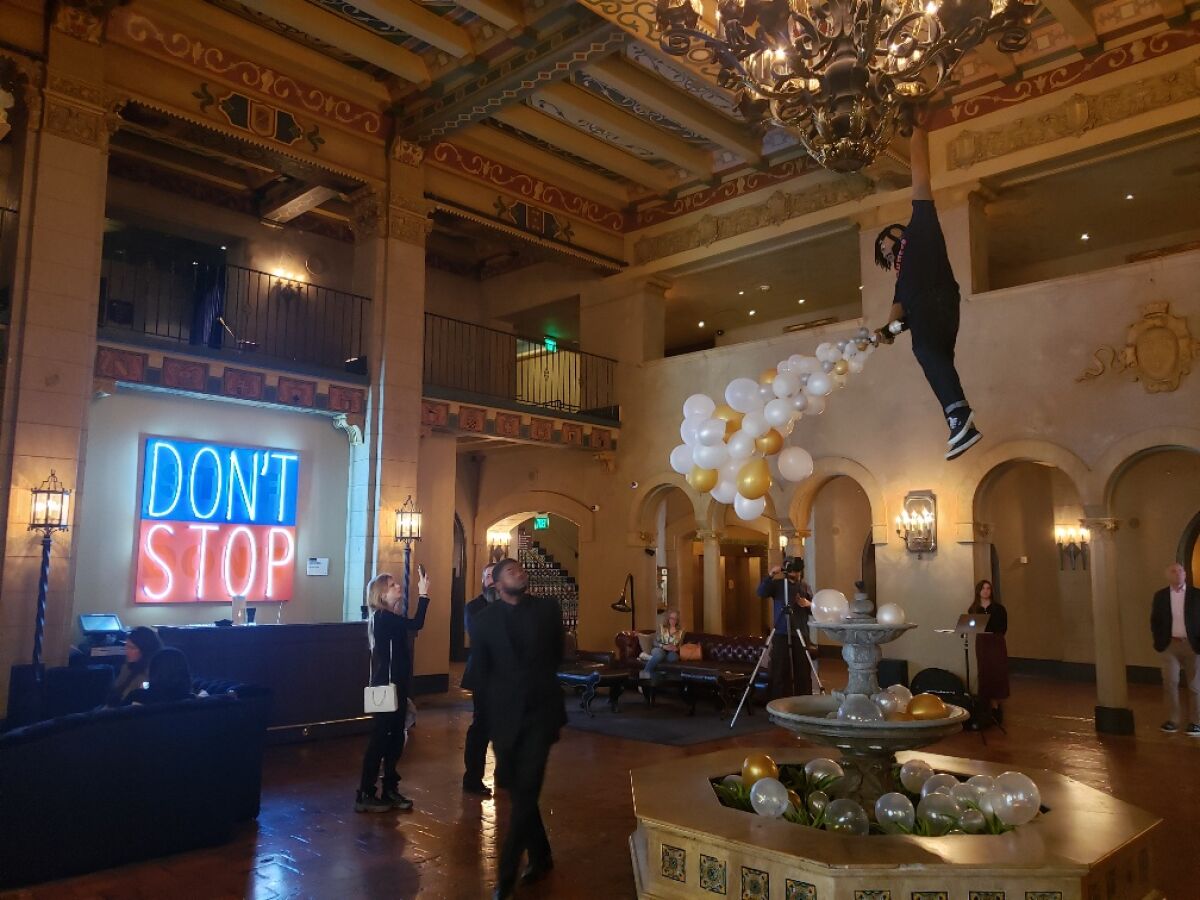 A neon sign by Deborah Kass and a chandelier/fountain sculpture of a dangling man by Luis Flores are in the Hollywood Roosevelt lobby for the Felix art fair.