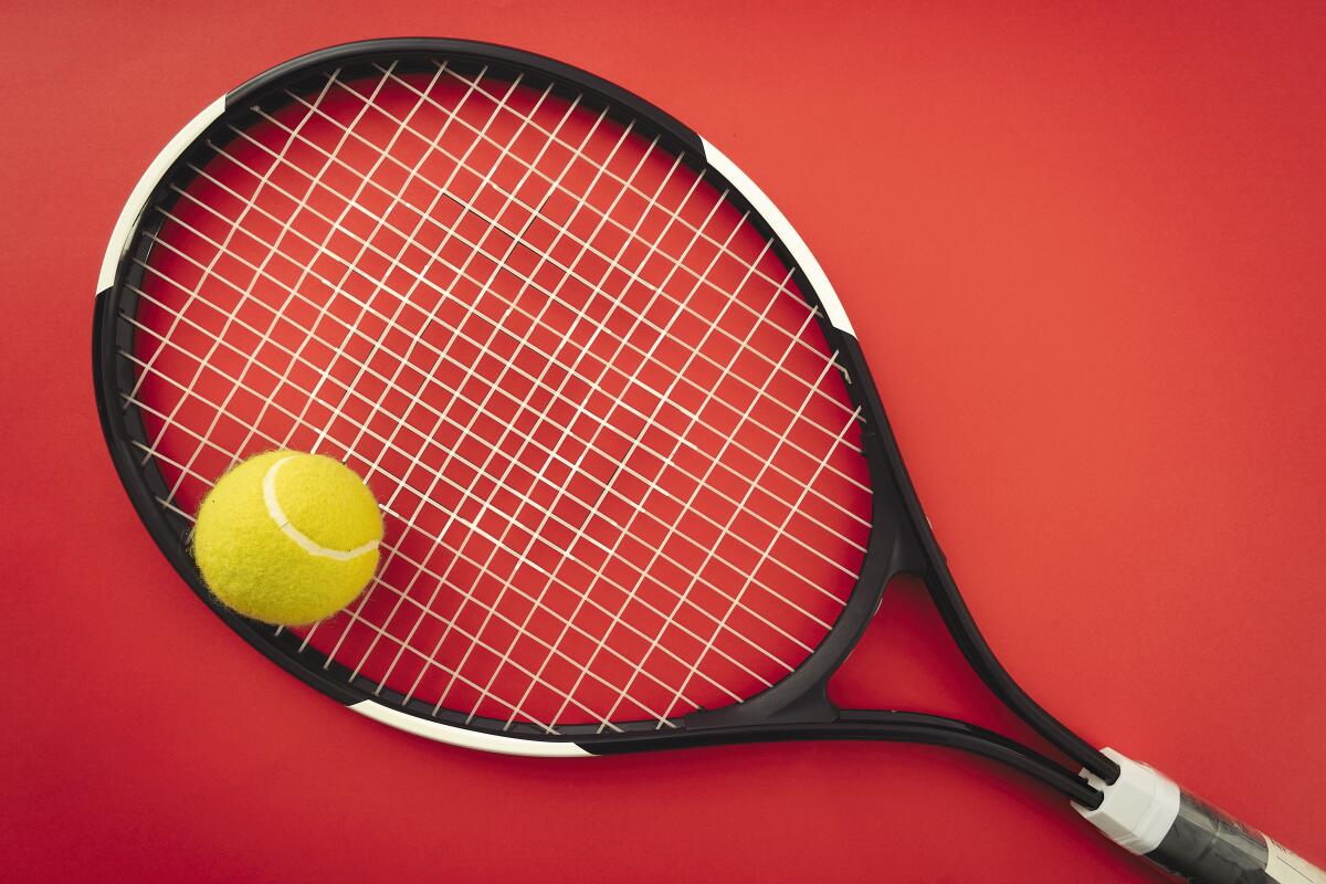 Tennis racket and tennis ball on the red court.