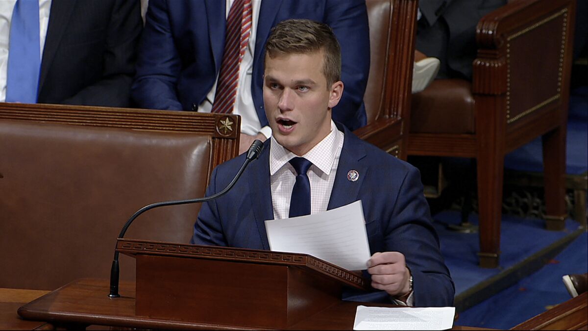 A man in a blue suit and dark tie holds a piece of paper as he speaks at a lectern