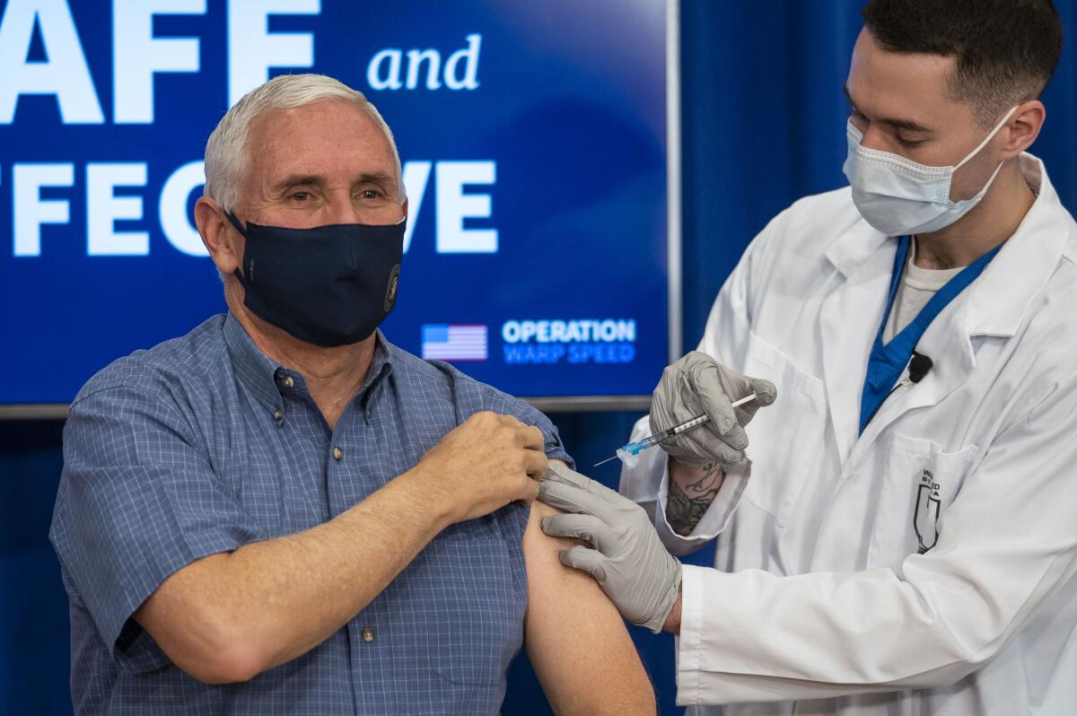 A doctor in a mask prepares to inject a vaccine into Mike Pence's arm at the White House