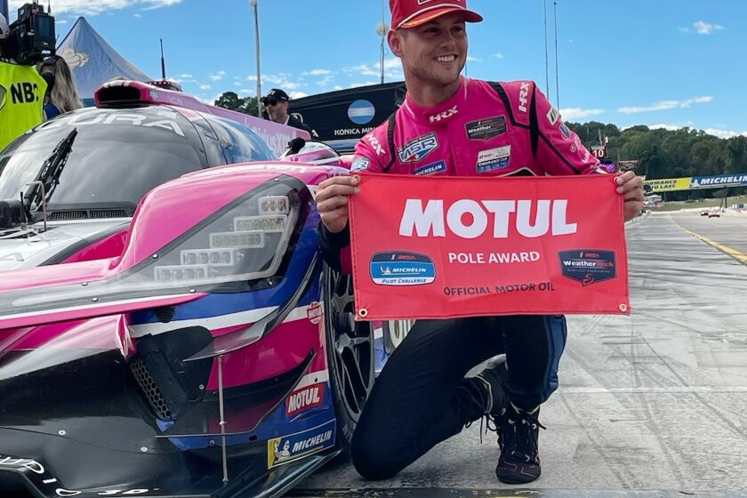 Tom Blomqvist, of Meyer Shank Racing, poses with flag after qualifying for the pole position, Friday, Sept. 30, 2022, in the IMSA sports cars season-ending Petit Le Mans auto race at Road Atlanta in Braselton, Ga. The team goes into Saturday's race second in the championship standings. Ensuing pictures show teammate Helio Castroneves congratulating Blomqvist, team owner Mike Shank and drivers Helio Castroneves and Oliver Jarvis watching Blomqvist qualify. (AP Photo/Jenna Fryer)