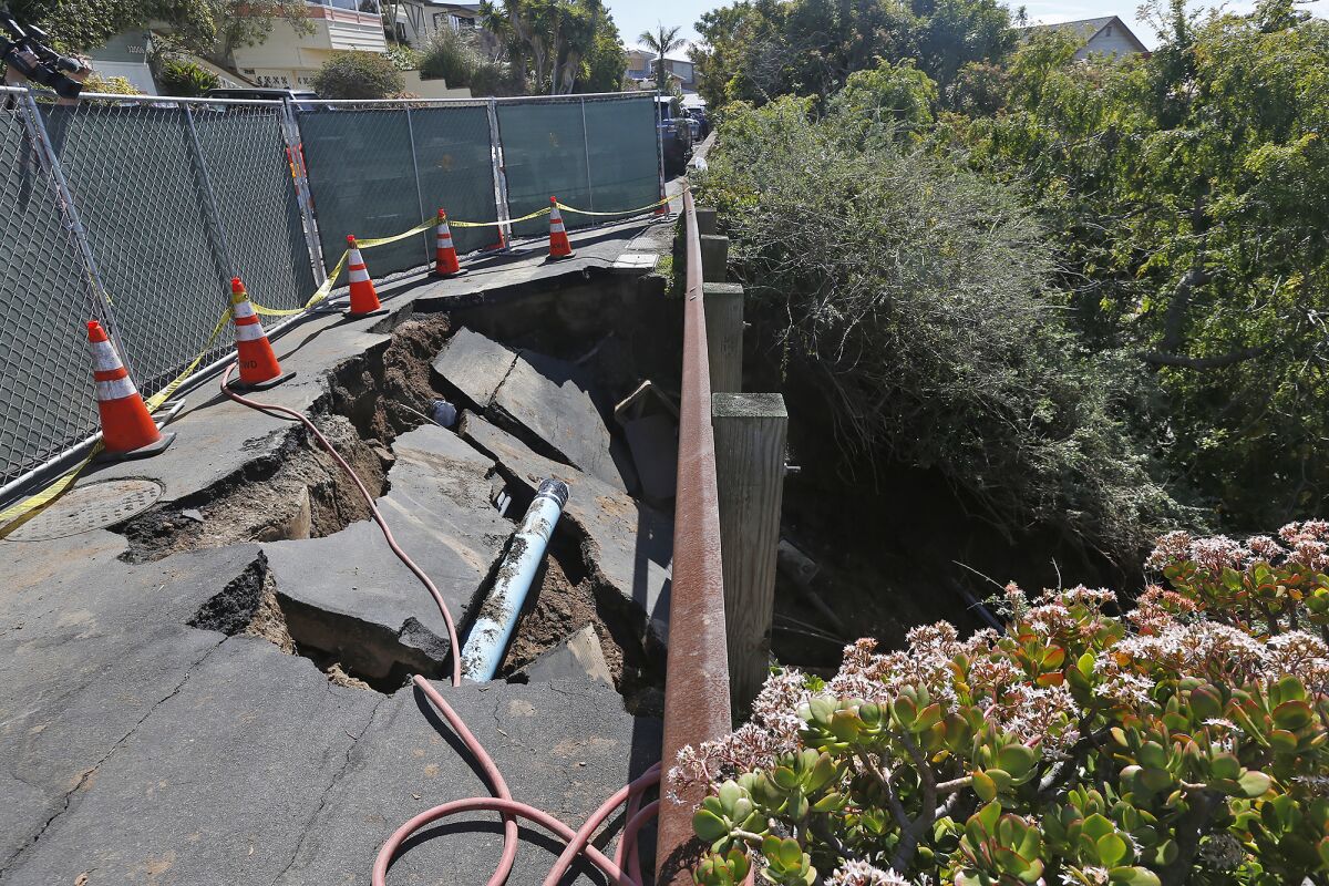 Cones and a fence around a sinkhole that caved in the side of a street on a hillside