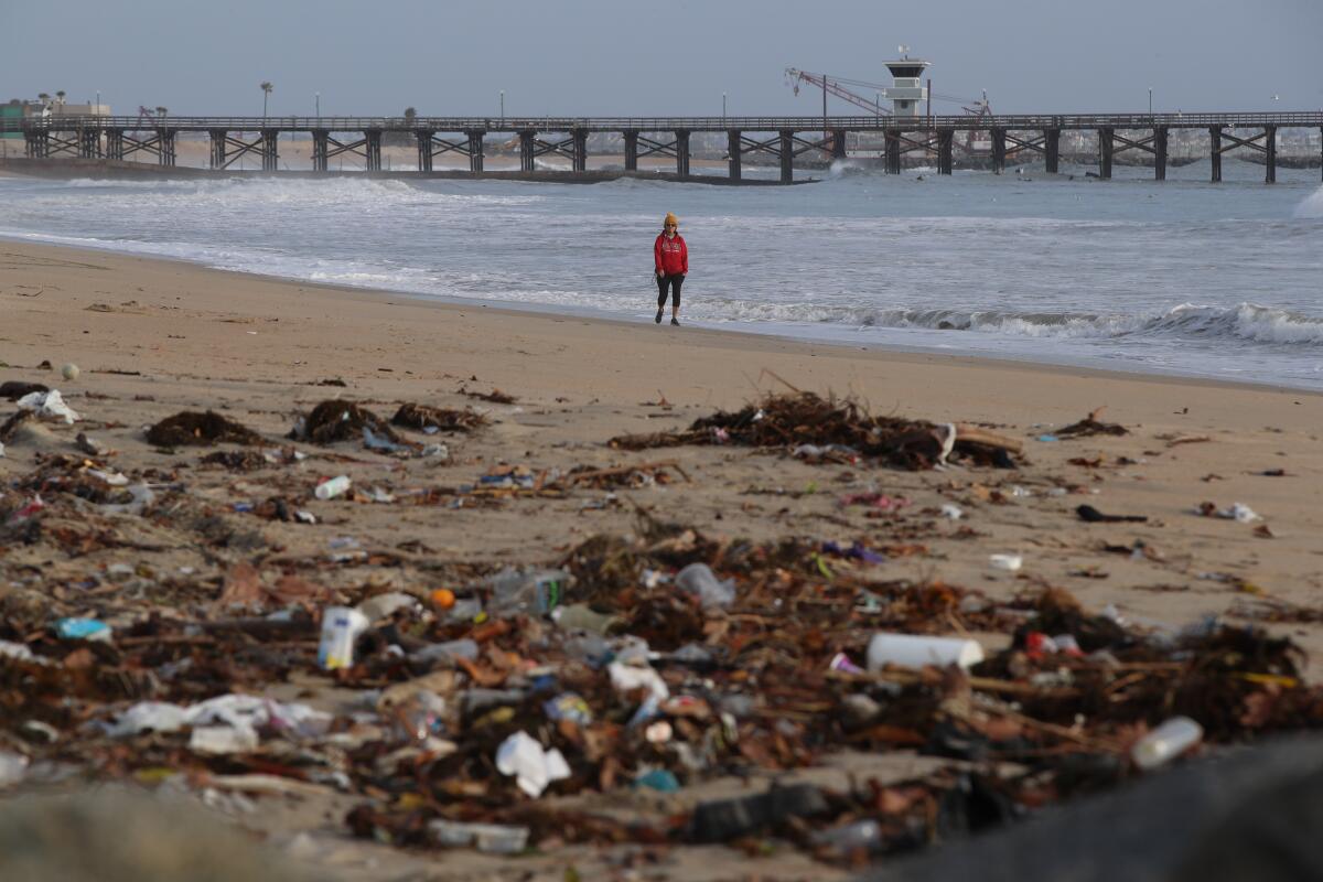 A beachgoer walks past trash and debris from recent storms on Seal Beach.