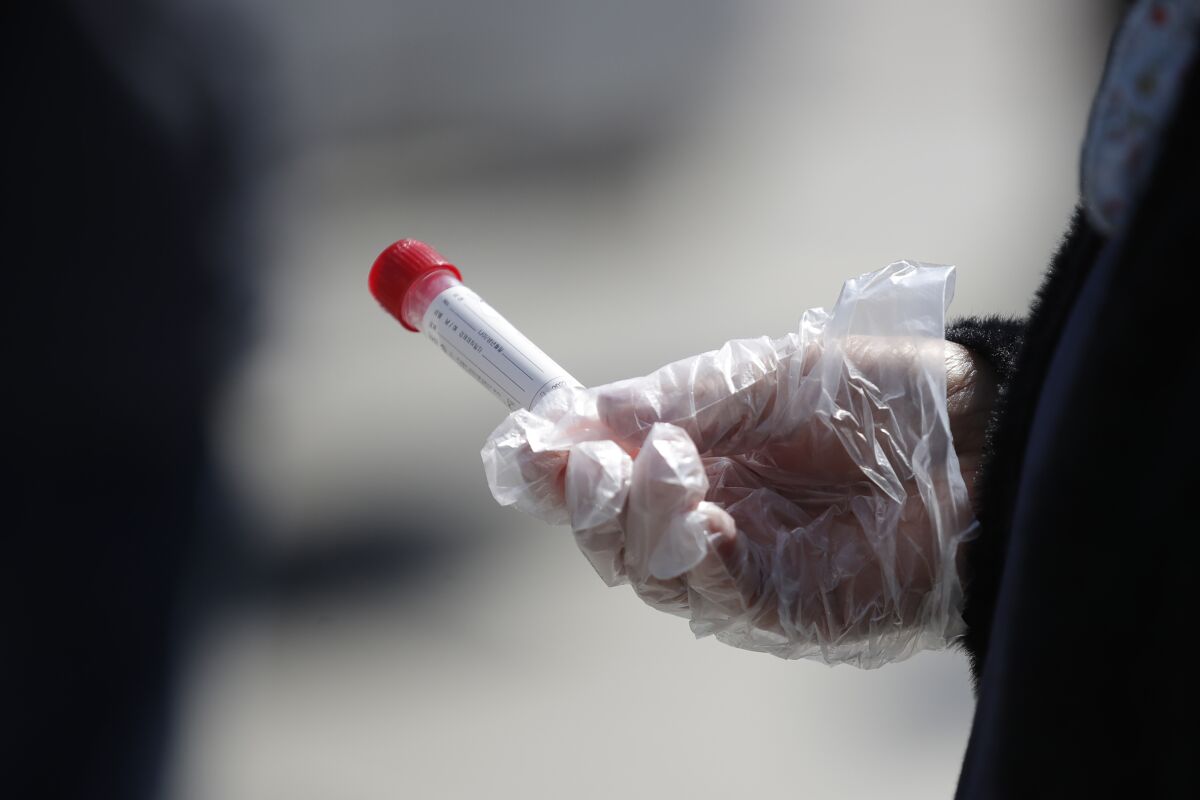 A woman wearing a glove holds a vial as she waits in a line at a testing site in Seoul in April.