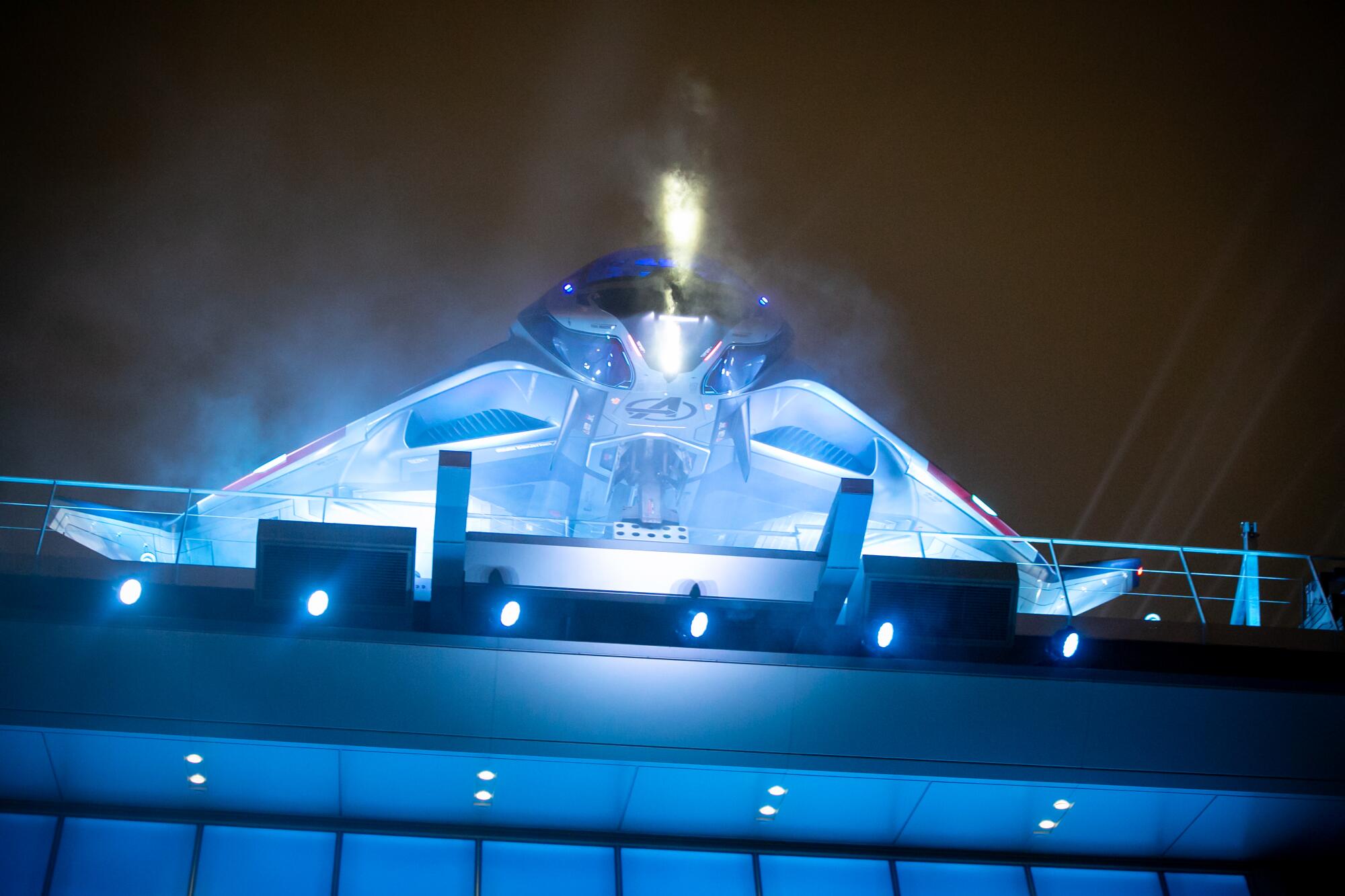 The Quinjet, illuminated with the Avengers logo, is docked on a high platform.