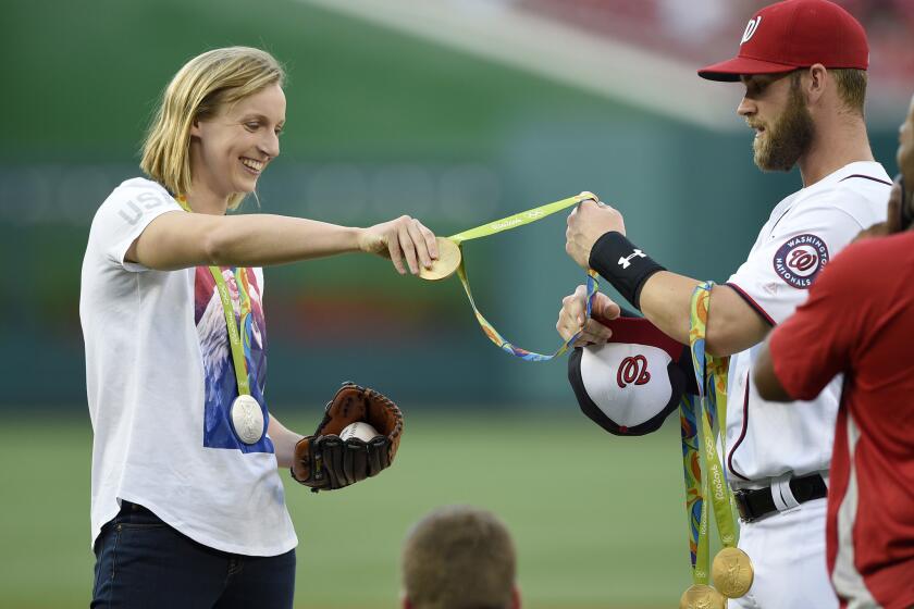 Katie Ledecky hands her Olympic medals to Washington Nationals' Bryce Harper.