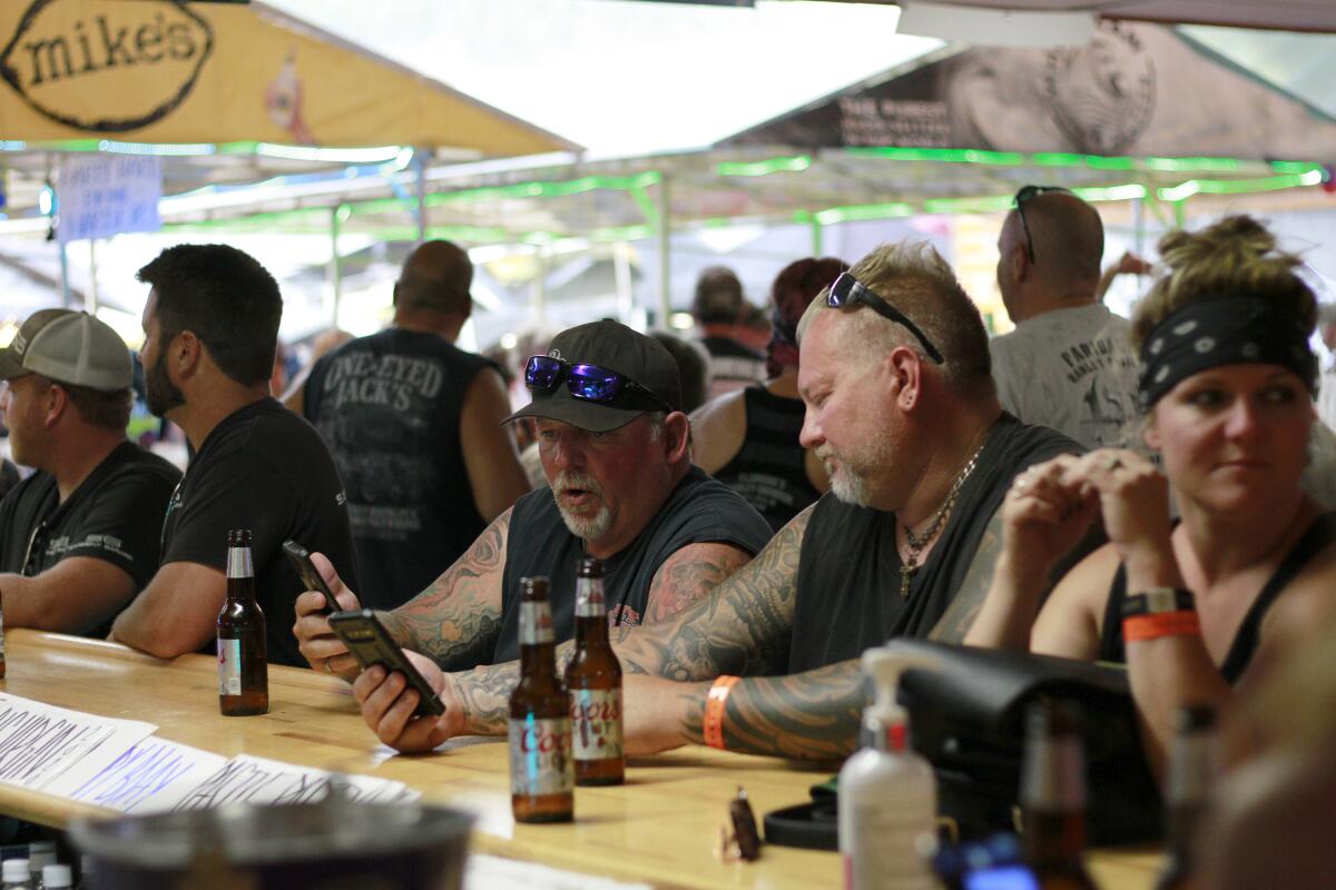 People sit at a bar drinking beers and looking at phones during the Sturgis Motorcycle Rally in South Dakota