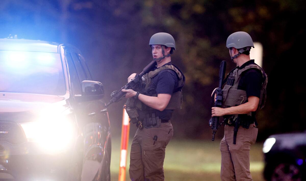Two law enforcement officers holding rifles next to a vehicle 