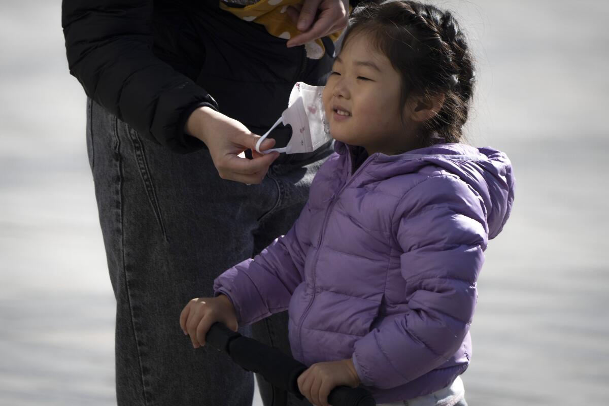 Una mujer le saca la mascarilla a una niña mientras juega en una plaza en Beijing