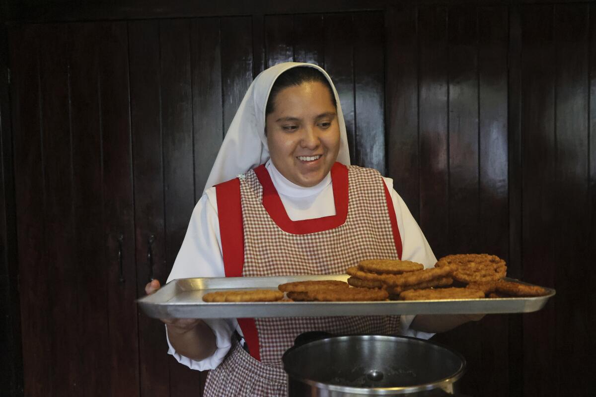 A nun holds a tray of baked goods.