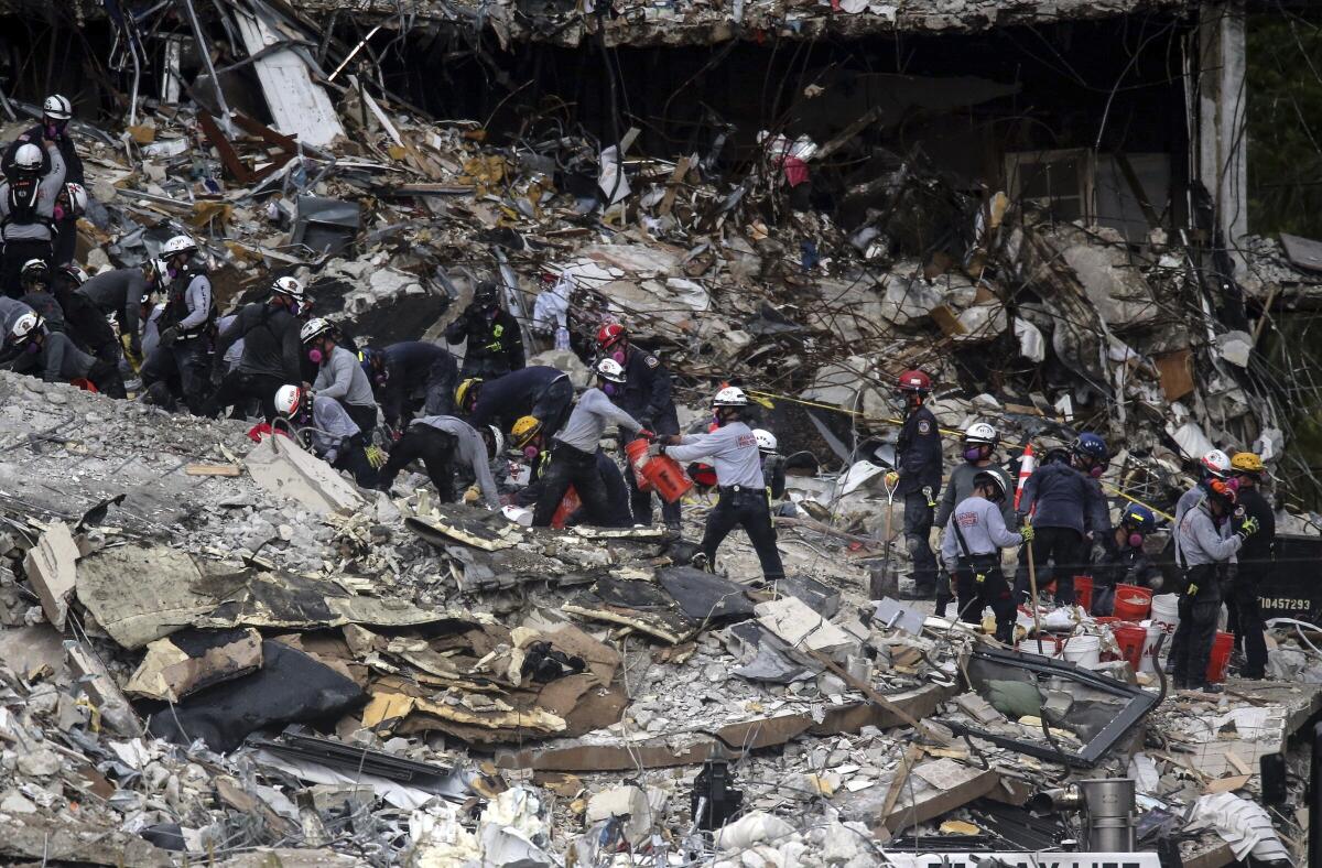 People wearing protective helmets work amid a mountain of debris.