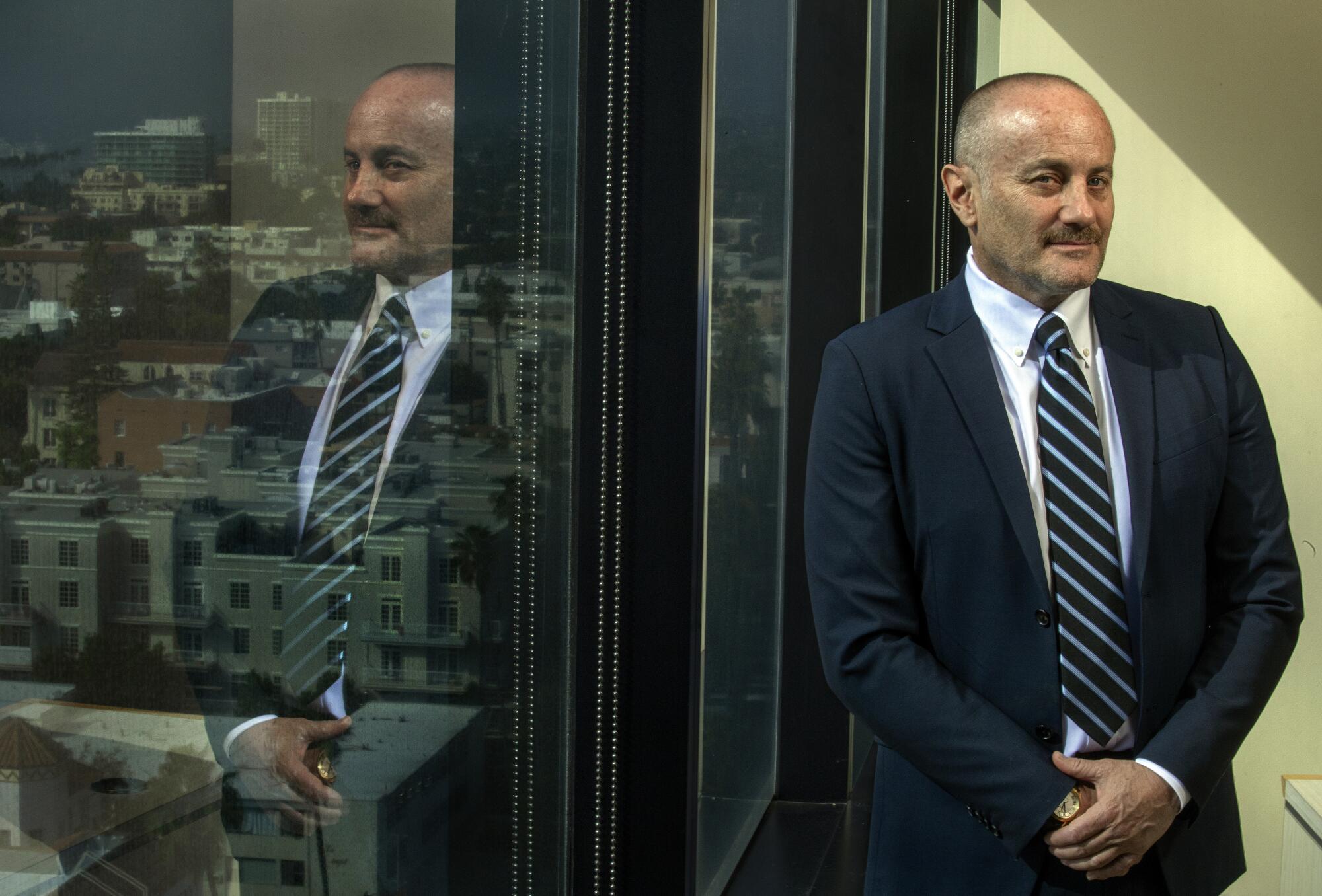 A man in a suit stands next to a window in an office building.
