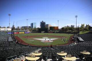 Players on a baseball diamond, seen from stadium seats, with buildings in the background