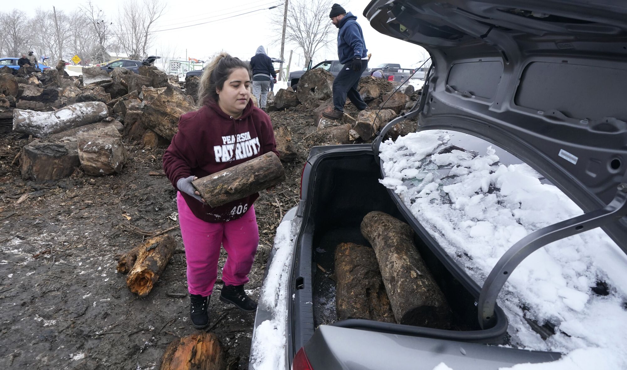 A woman loads firewood into a trunk.
