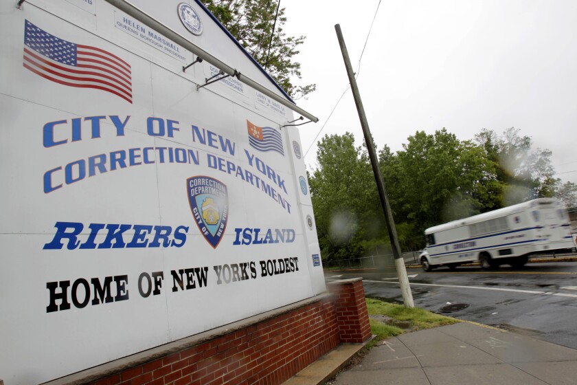 FILE - In this May 17, 2011 file photo, a New York City Department of Corrections bus passes the sign near the gate at the Rikers Island jail complex in New York. Four correctional officers at Rikers Island jail have been suspended without pay after they allegedly stood by and failed to stop a teenage inmate from hanging himself on Thanksgiving, leaving him hospitalized in intensive care. Nicholas Feliciano, 18, remained unconscious in a hospital prison ward Wednesday, Dec. 4, 2019 a week after he nearly died in his Rikers Island jail cell, according to the Legal Aid Society, the public defender organization that represents him in court. (AP Photo/Seth Wenig, File)