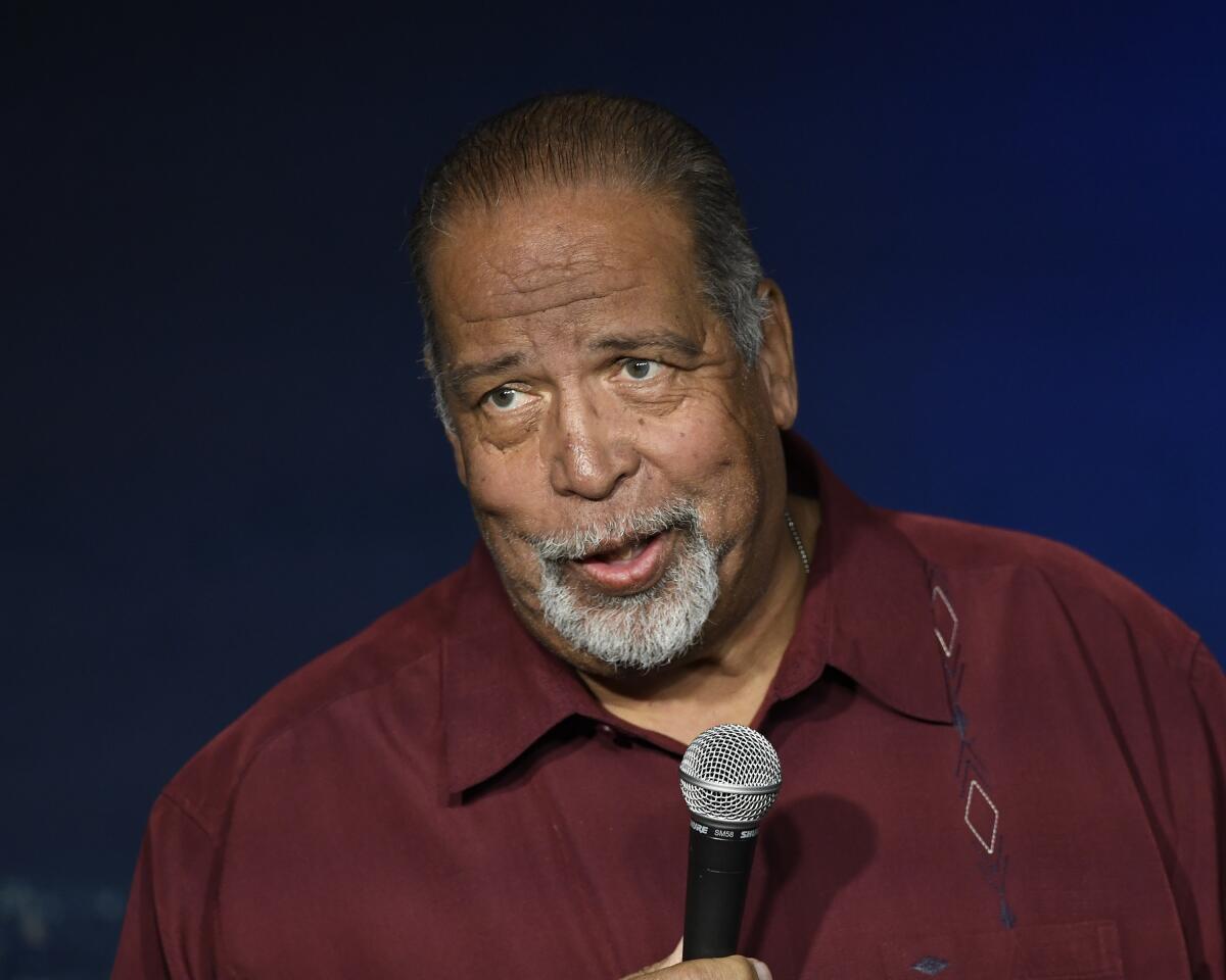 A bearded man in a burgundy shirt holding a microphone.