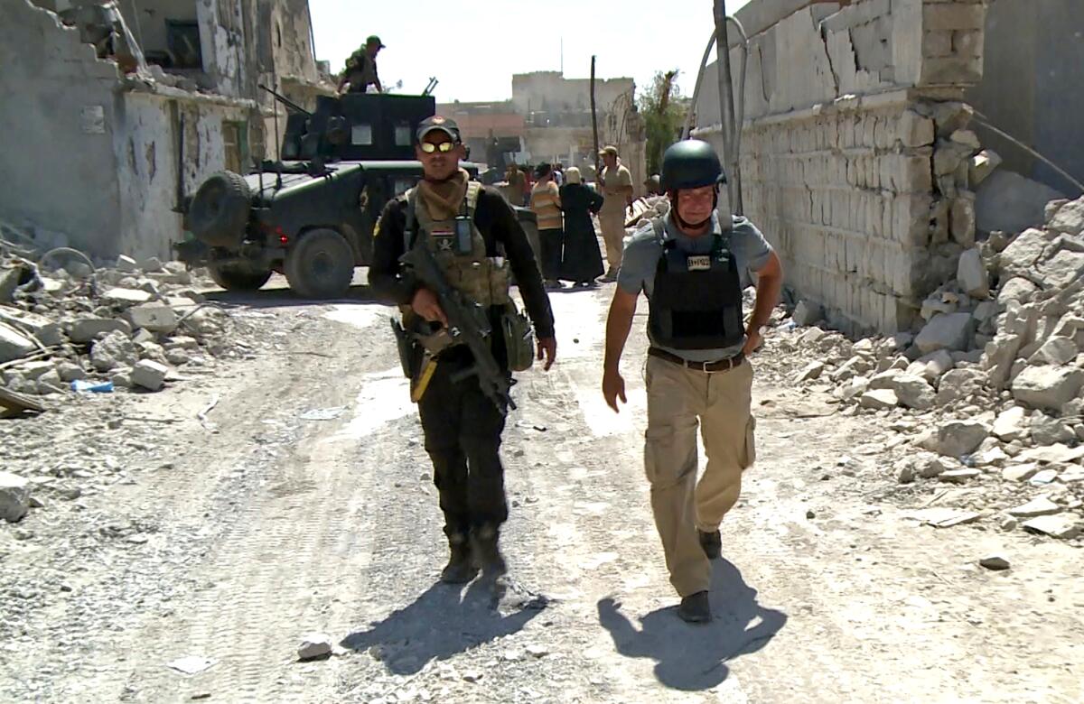 Two men walk down a road amid ruins in Iraq.