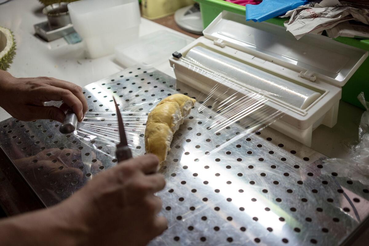 Tan Chee Wei wraps a section of durian to be vacuum-packed for a customer to take on a flight. (Suzanne Lee / For The Times)