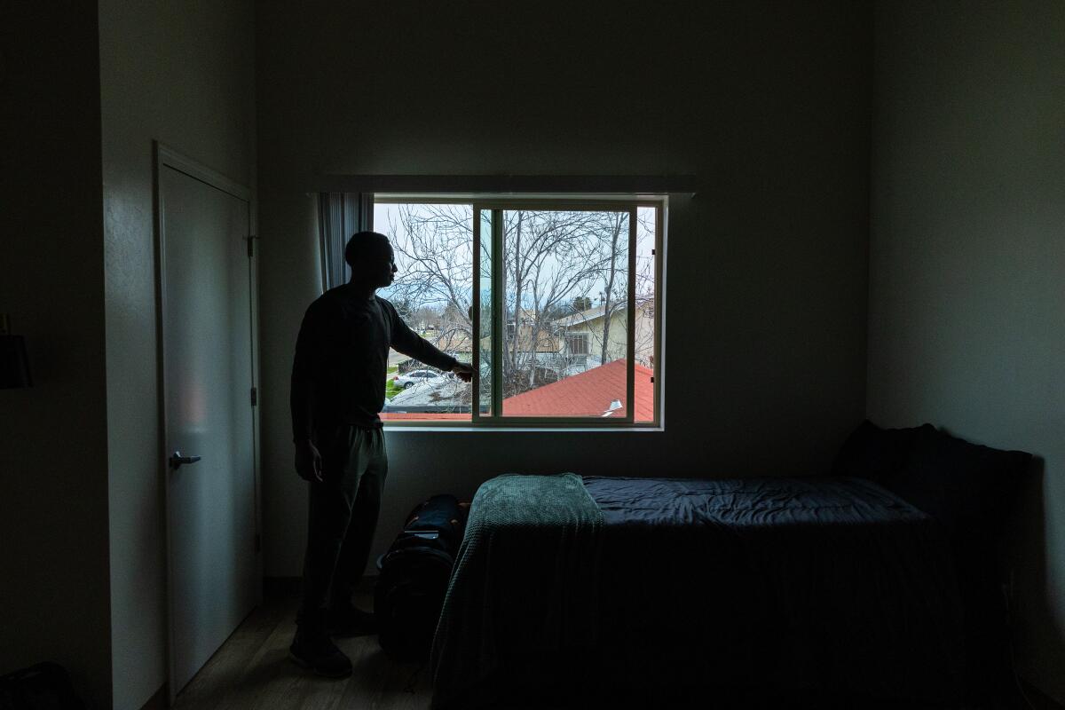 A young man opens the window of a tidy apartment. 