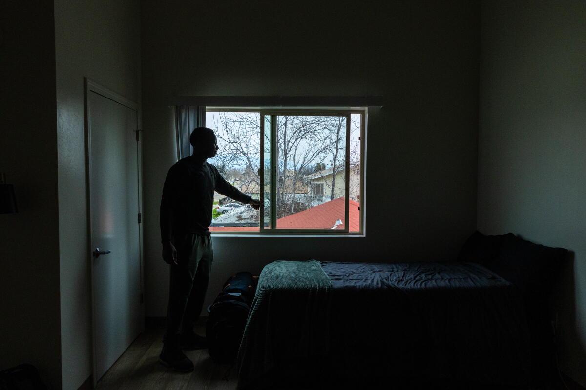 A young man opens the window in a tidy apartment.