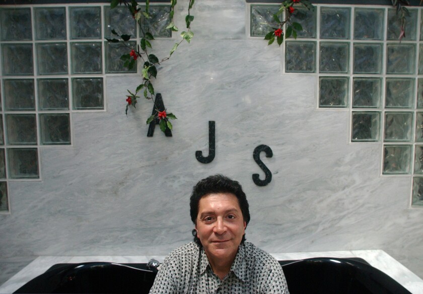 A man poses in a bathtub with the letters "AJS" on the wall behind him.