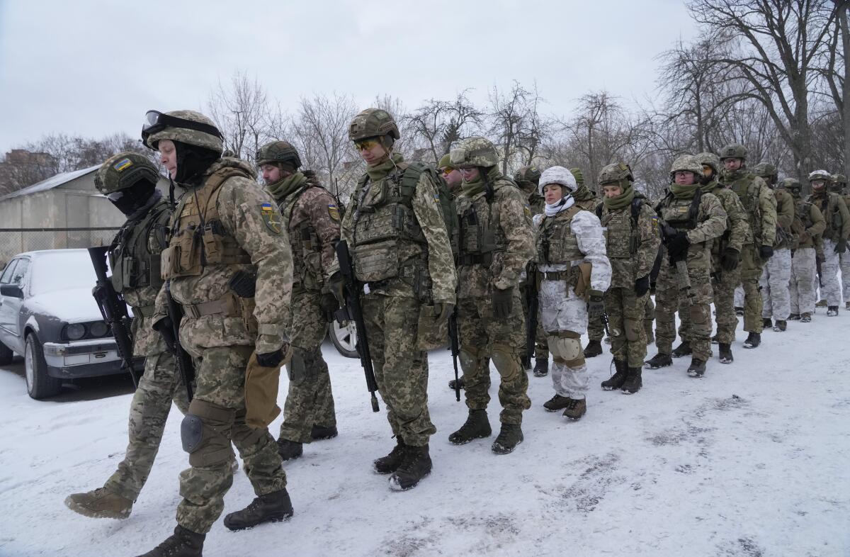 Armed people in uniforms line up in a snowy park 