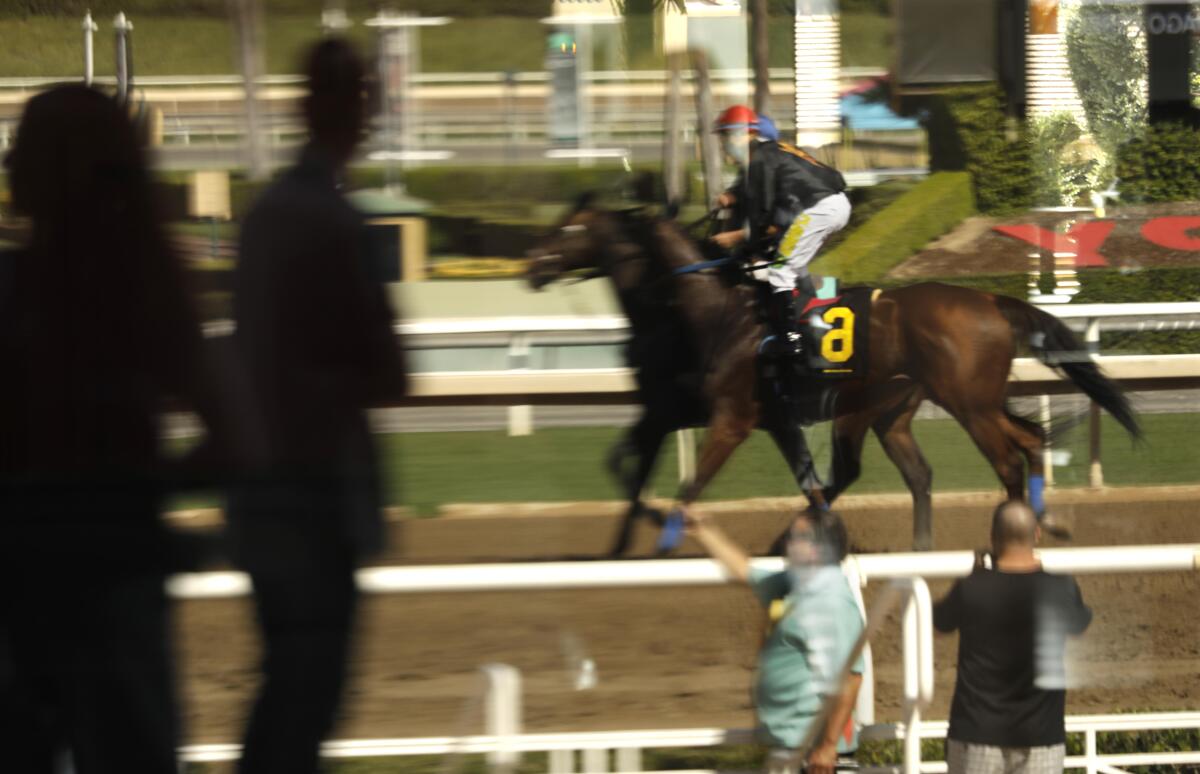 Jockey Tyler Baze, No. 6, in a reflection, rides onto the track for the third race on opening day at Santa Anita.