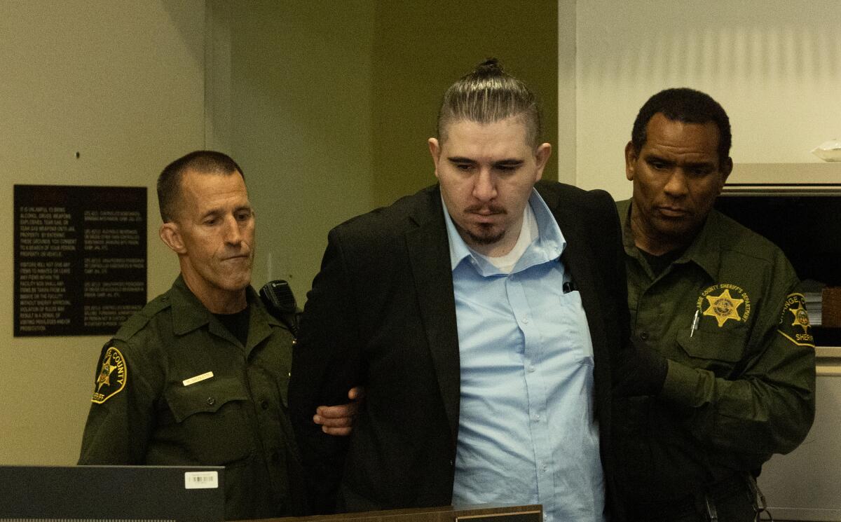 A man is escorted by sheriff's bailiffs to his seat in a courtroom