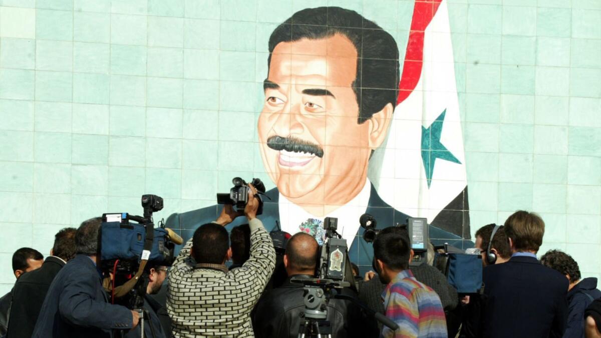 Foreign and local cameramen crowd in front of a mural of Iraqi President Saddam Hussein in 2002.