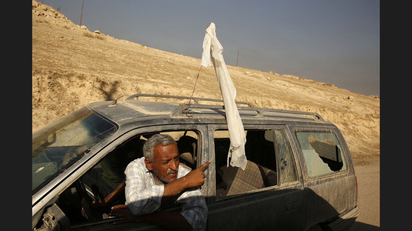 A man flying a white flag with his rear window shattered, is stopped on the road from Salhiya to Qayarrah.