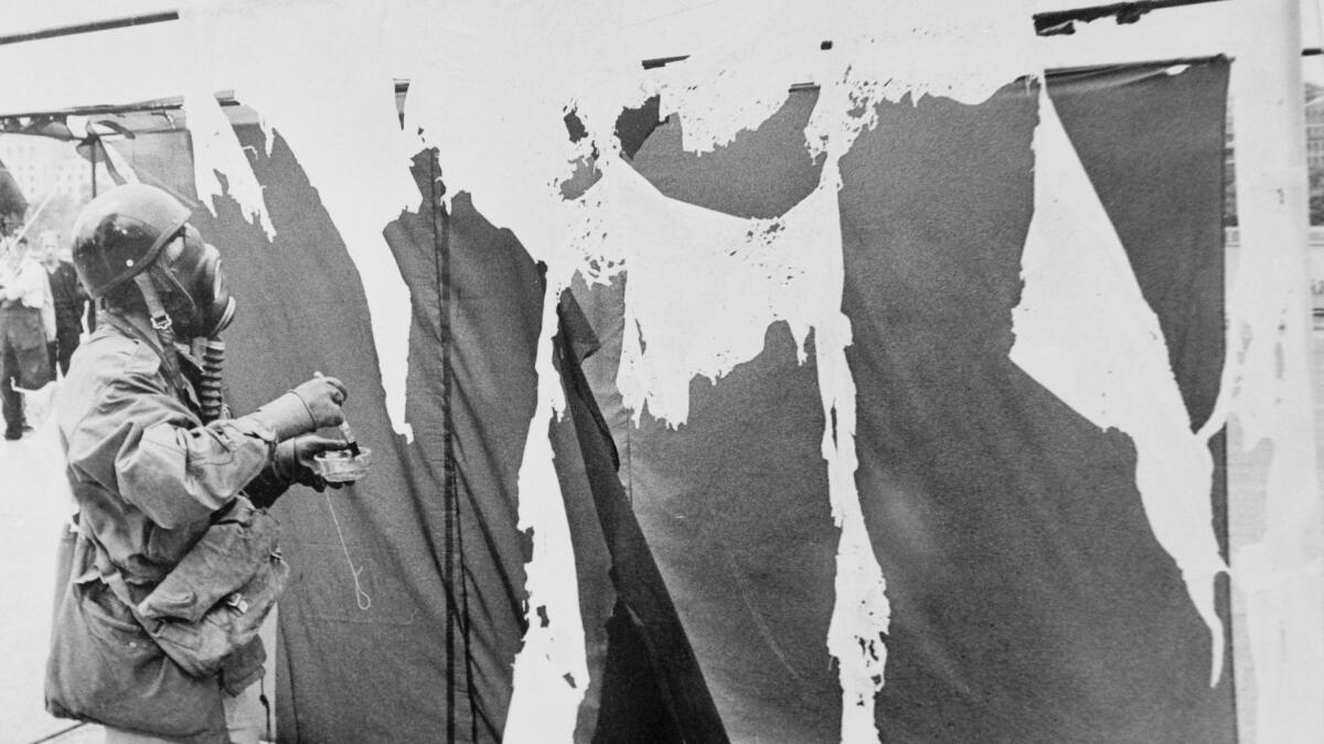 German performance artist Gustav Metzger, founder of the "auto-destructive" school of art, wears a gas mask in 1961 while painting three nylon curtains with acid, causing them to disintegrate.
