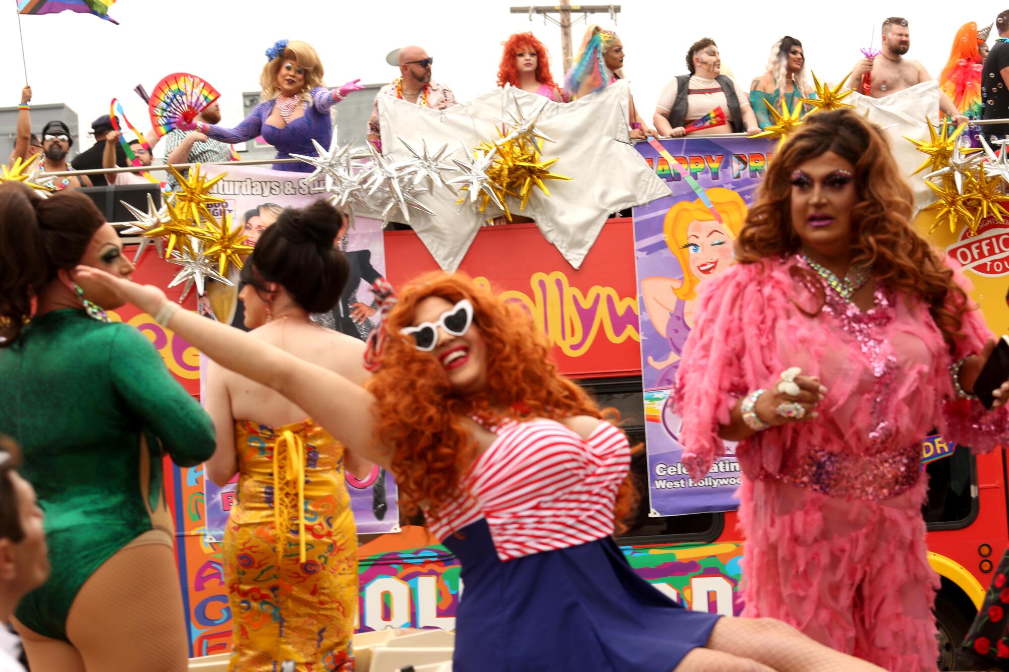 A drag queen in heart-shaped sunglasses and striped red, white and blue outfit leans back in a pose.