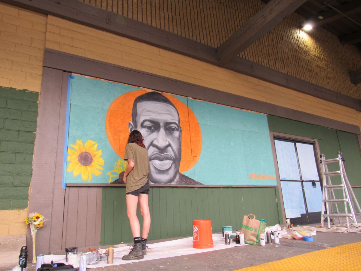 Artist Chloe Becky is shown working on a mural featuring George Floyd at the La Mesa Springs Shopping Center. 