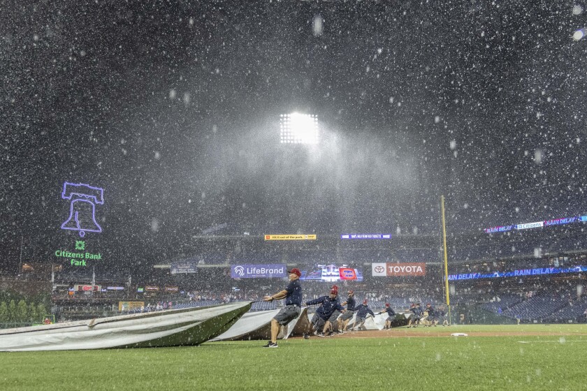 Grounds crew members cover the field during a rain delay in the 10th inning of a baseball game between the Philadelphia Phillies and the Miami Marlins, Saturday, July 17, 2021, in Philadelphia. (AP Photo/Laurence Kesterson)
