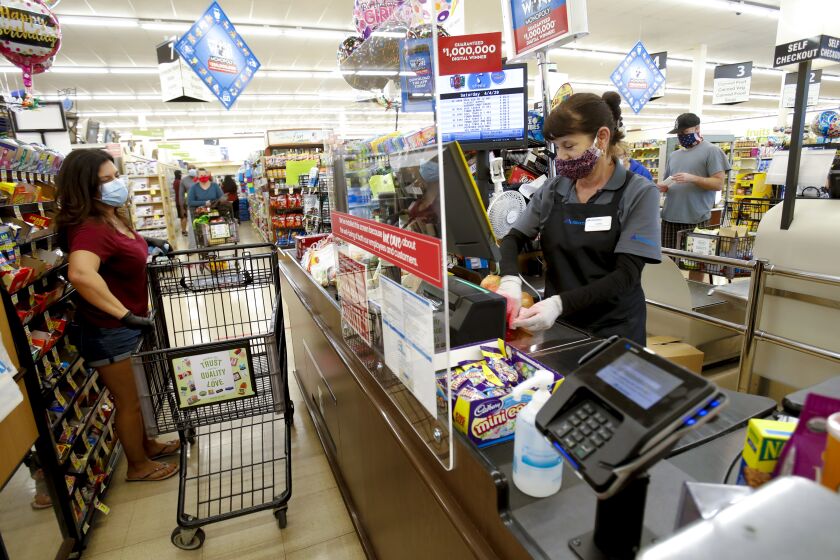 Dora Macias a cashier at the Albertsons in San Carlos rang up Gina Springer's groceries on Saturday. Effective midnight Friday all employees at grocery stores are required to wear a cloth covering their face. This is an added measure of precaution on top of the earlier required sneeze guards installed late in March.