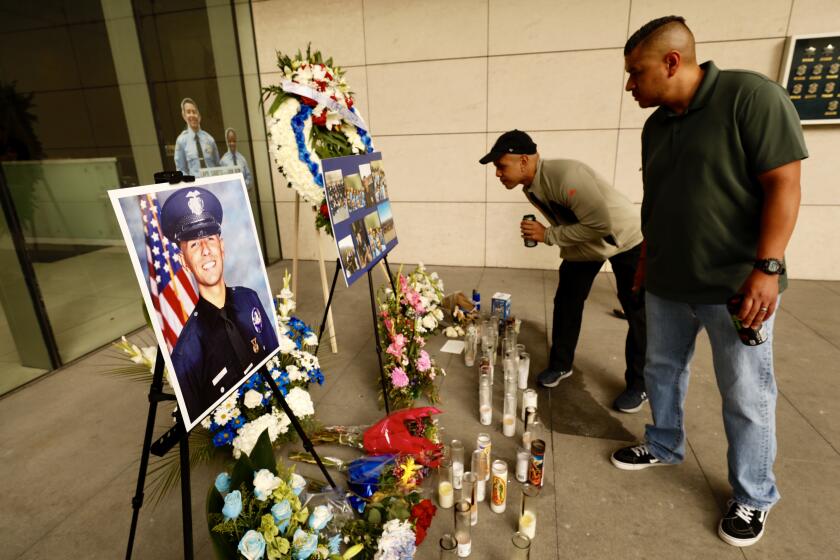 Chris Martin, center, and Ricardo Camacho visit a memorial to slain LAPD officer Juan Diaz, in front of LAPD headquarters. Camacho’s parents were godparents to Diaz.