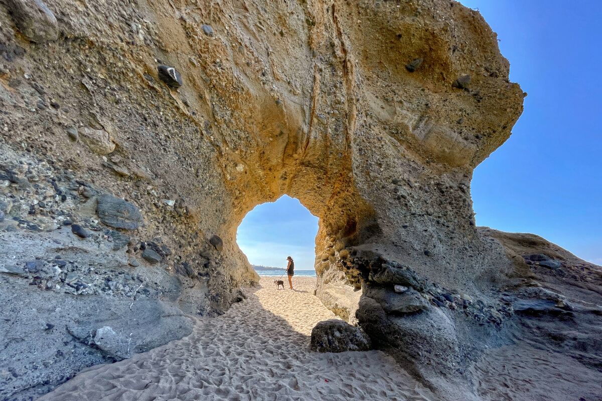 A person and a dog are framed by a rock arch.
