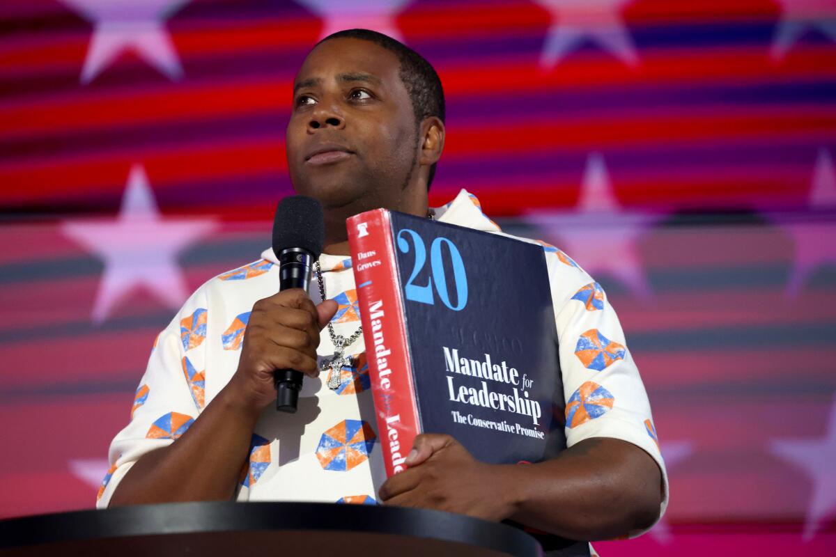 Comedian and actor Kenan Thompson holds a giant copy of the Heritage Foundation's Project 2025 