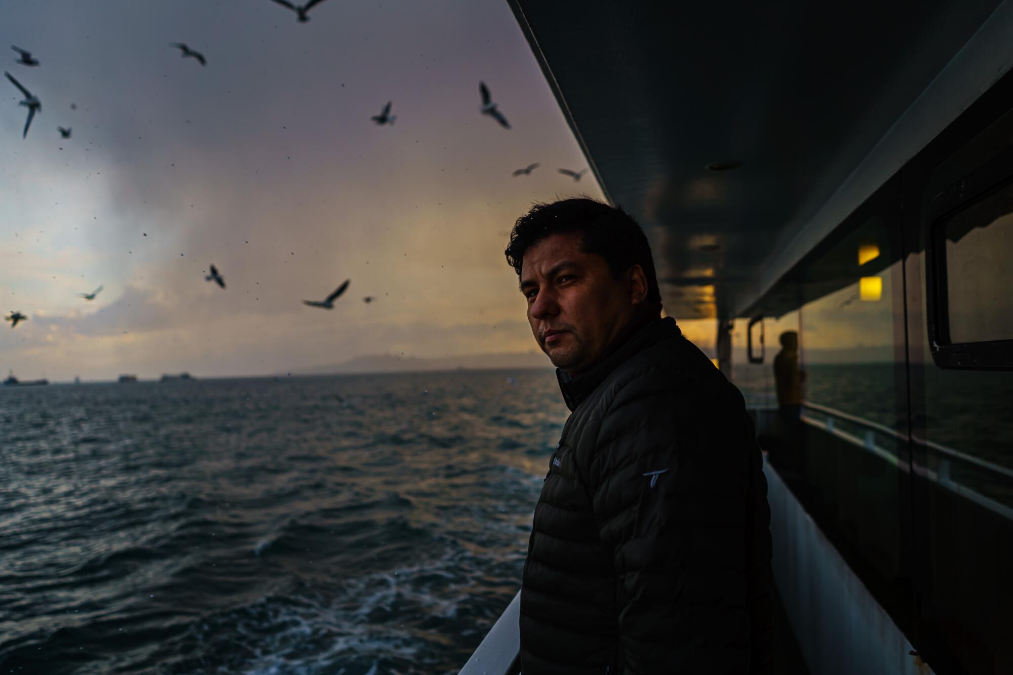A man stands on a ferry, with the ocean and sky as a backdrop