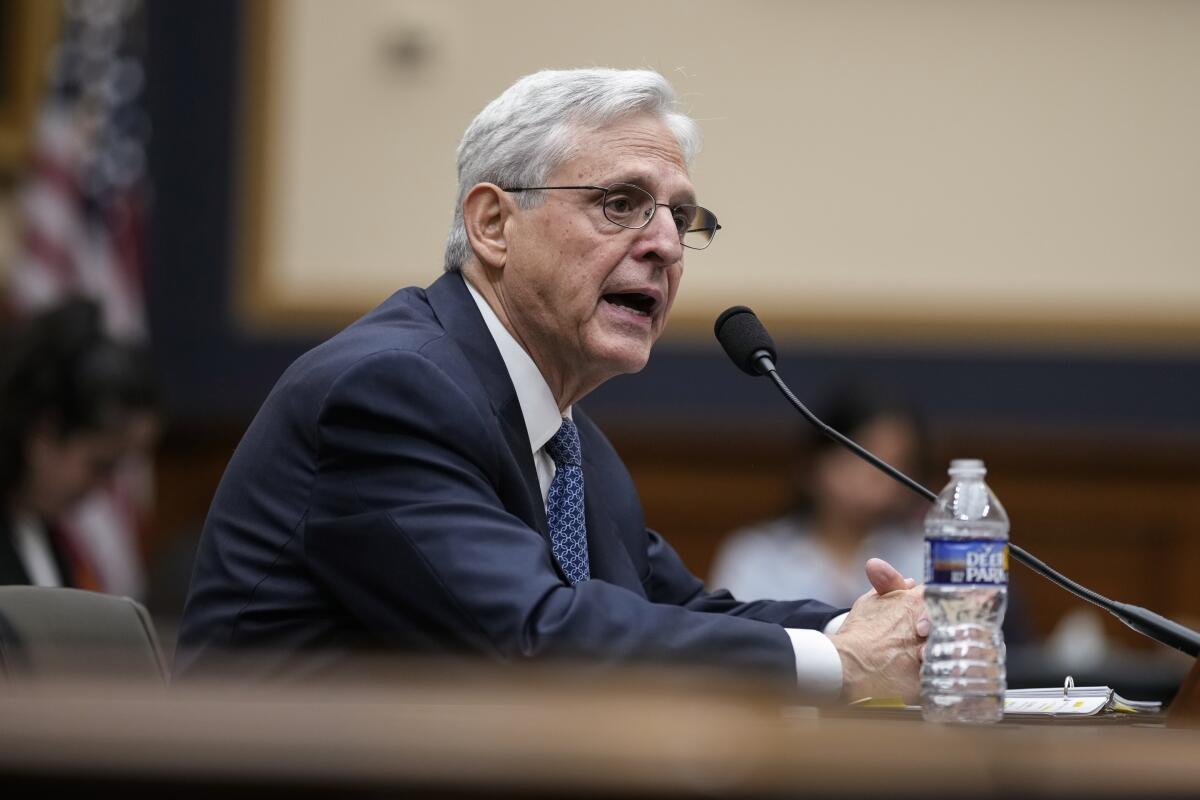 Atty. Gen. Merrick Garland sitting at table, speaking into a microphone