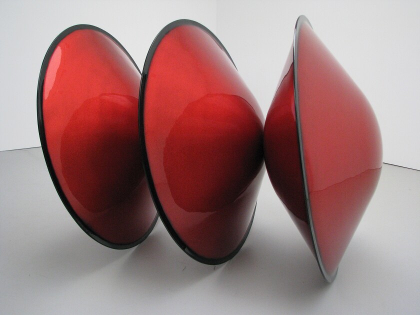A sleek sculpture made from three conjoined disk shapes is painted in shiny red automotive paint.