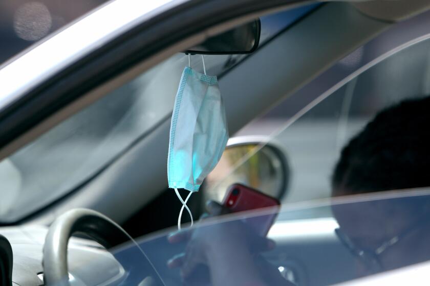 A woman about to fill her gas tank at the ARCO station has a mask hanging from her rearview mirror, on Foothill Blvd. in La Canada Flintridge on Tuesday, April 14, 2020.