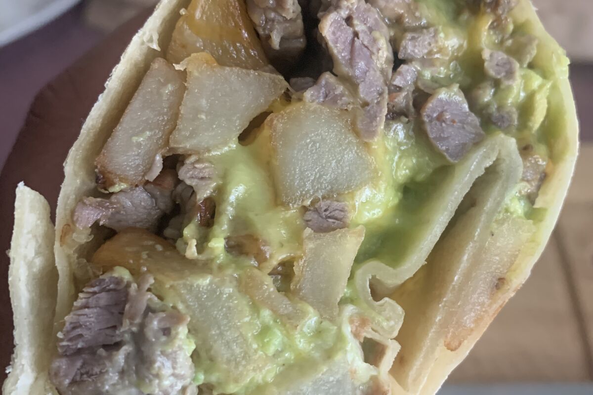 cross section of burrito with breakfast potatoes, carne asada and guacamole