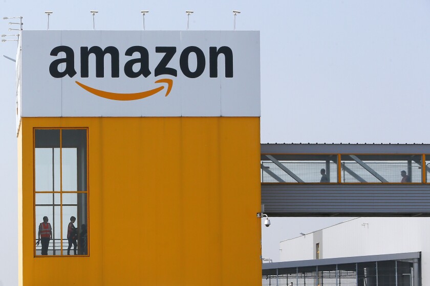 FILE - In this April 9, 2020, file photo, employees observe social distancing due to coronavirus, at the entrance of Amazon, in Douai, northern France. Amazon announced Tuesday, Feb. 2, 2021, that Jeff Bezos would step down as CEO later in the year, leaving a role he’s had since founding the company nearly 30 years ago. (AP Photo/Michel Spingler, File)