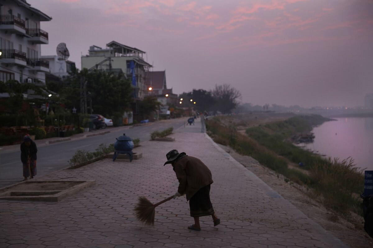 FILE - m municipal worker sweeps a pathway along the Mekong River Thursday, Dec. 12, 2013, in Vientiane, Laos. The landlocked Southeast Asian nation of Laos reopened to tourists and other visitors on Monday, more than two years after it imposed tight restrictions to fight the coronavirus. (AP Photo /Manish Swarup, File)