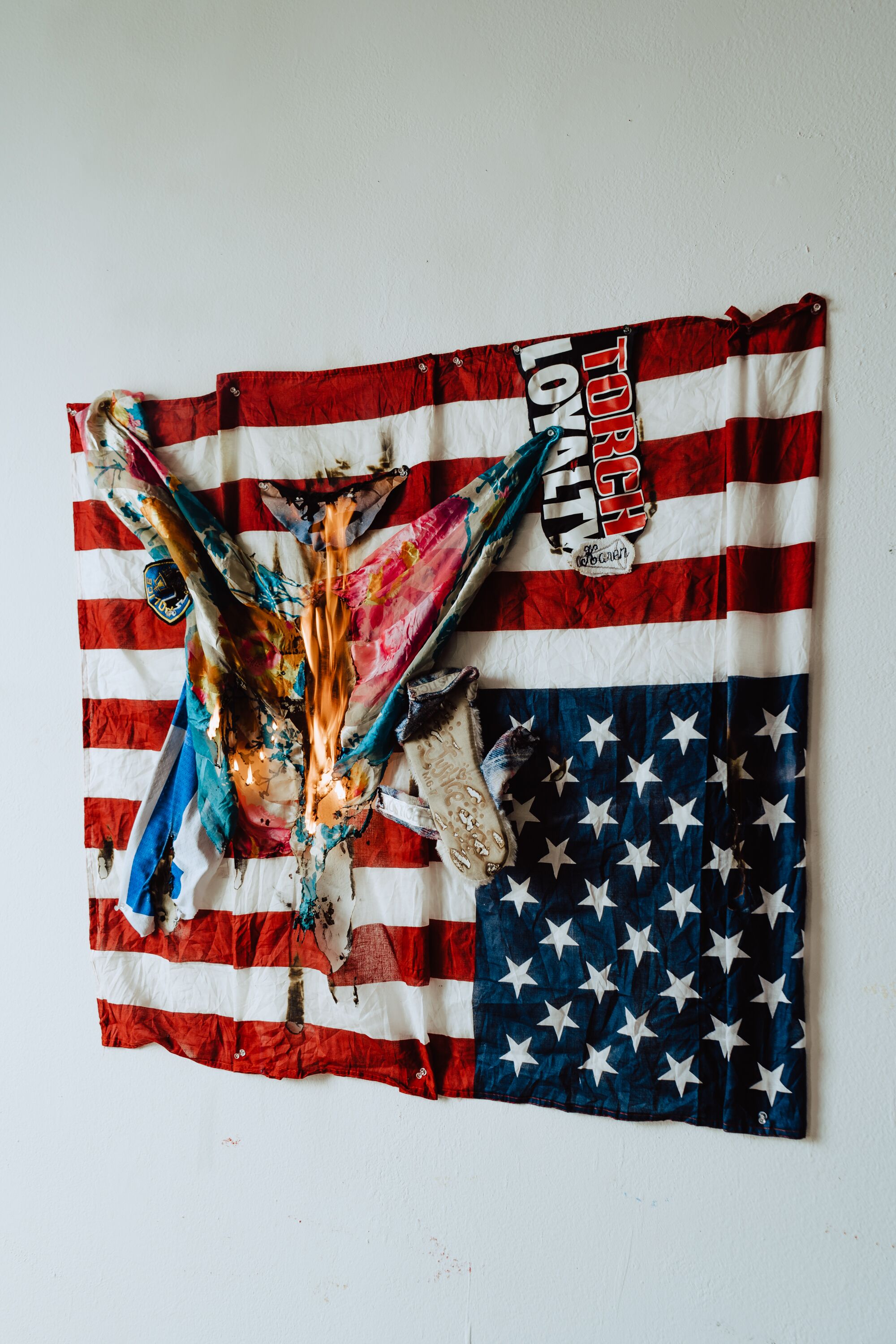 Muna Malik Recycled Democracy Found materials collage 37 x 35 U.S Flag, slipper, t-shirt, police patch