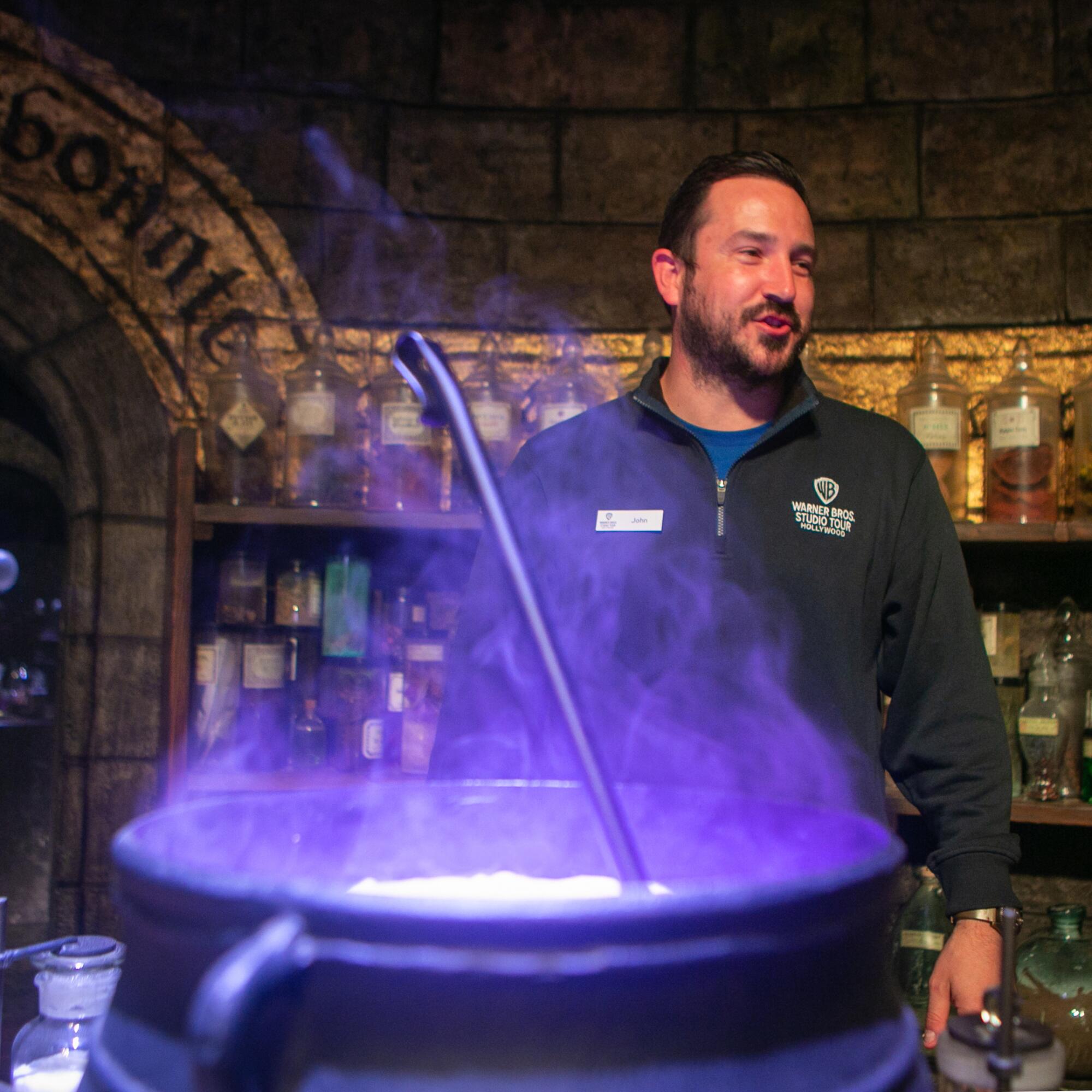 A man stands behind a cauldron that is glowing purple.