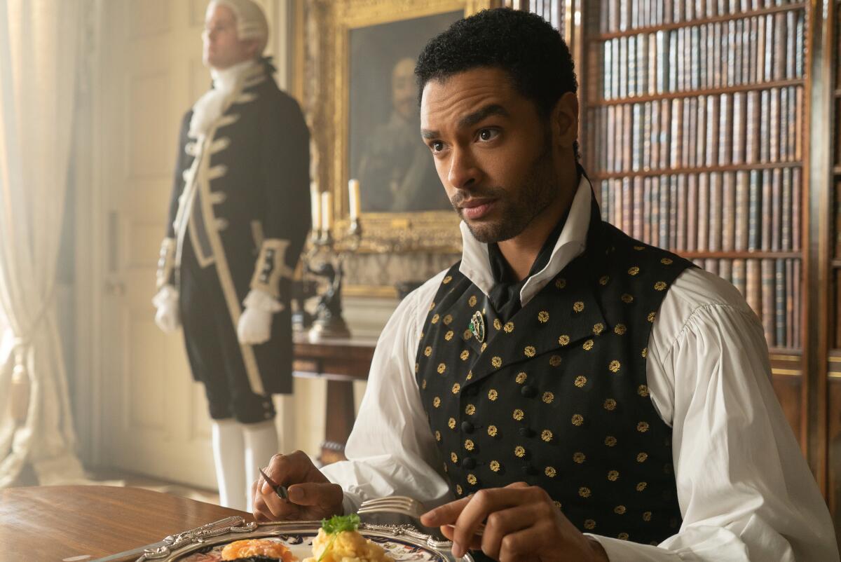 Regé-Jean Page holding utensils while sitting down for a meal in "Bridgerton"