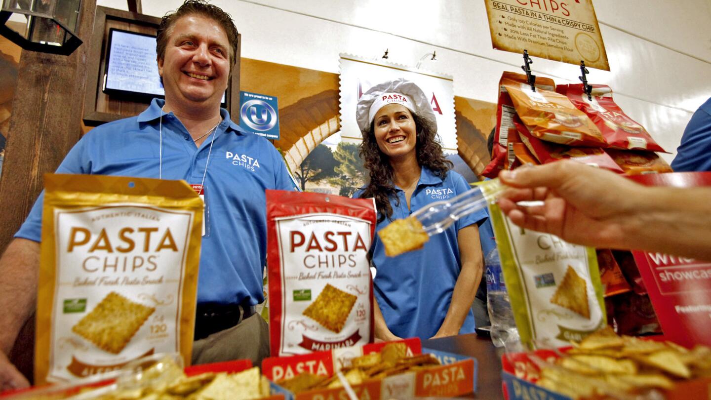Jerry Bello, CEO and founder of Pasta Chips, left, and marketing team member Corintha Collins smile as a person takes a sample of their product.