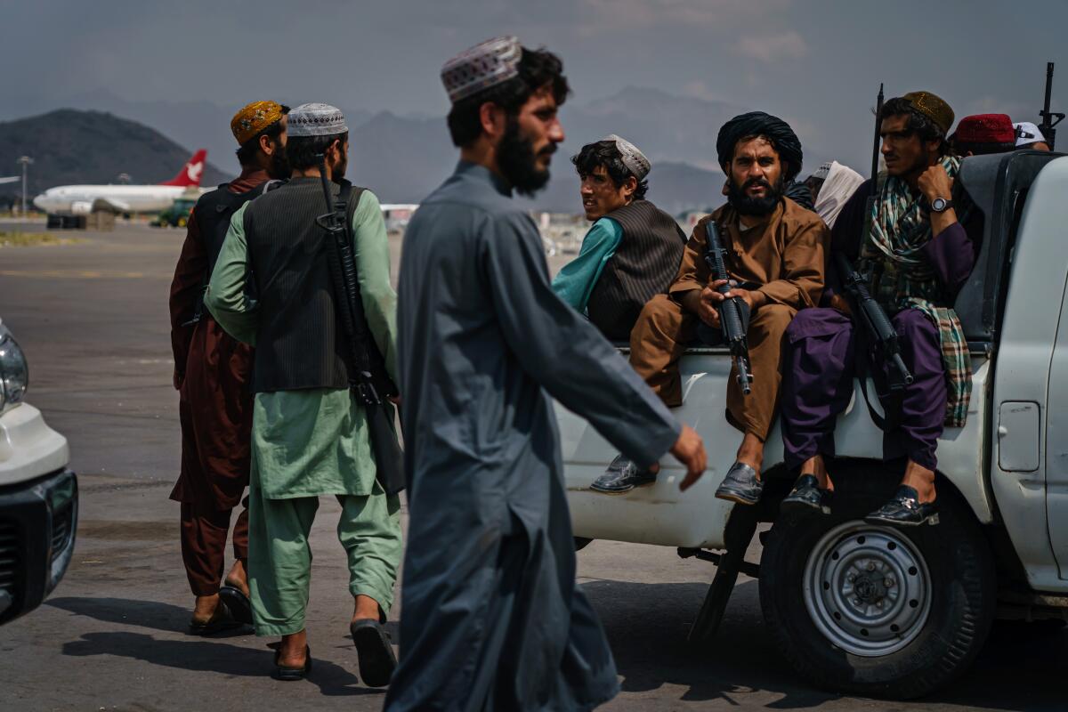 Armed men in tunics sit in the back of a truck while others stand nearby 